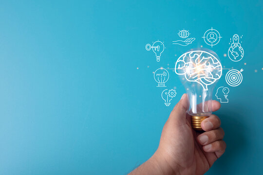 Hand holding a lightbulb with a glowing digital brain and business strategy icons on a blue background. Concept of artificial intelligence, creative idea, innovation, and smart technology.