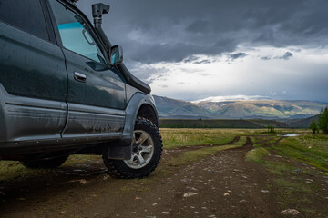 Side view of an off-road suv car parked on a muddy dirt road in a vast mountain valley under a dramatic stormy sky, overlanding and road trip adventure concept © ANDREY