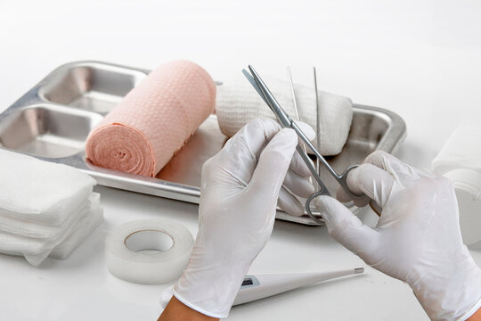Medical first aid supplies with bandages, gauze, scissors, forceps, gloves, and thermometer prepared for wound care and healthcare treatment on a clean white background.