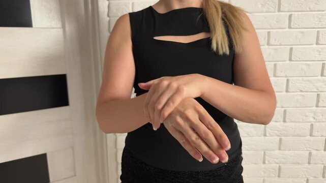 Woman rubbing lotion across hands and forearms indoors, with brick wall background, soft light, skincare routine detail, visible product sheen, clean wellness presentation