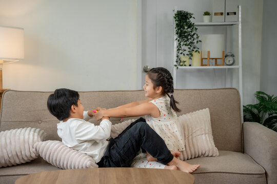 Children siblings playfully pulling toy on living room couch
