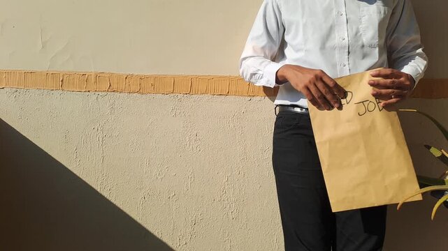 A job seeker wearing a white shirt and black pants holding a brown envelope with a handwritten need job text. Unemployment, career, and recruitment stock video footage.