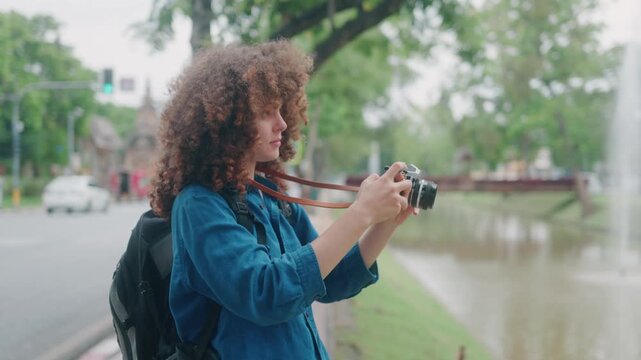 Young Female Traveler with Curly Hair Photographing with Film Camera in Asian City Park