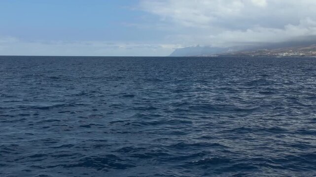 Calm Atlantic Ocean under a cloudy sky with distant island coastline barely visible on the horizon in the Canary Islands, Spain.