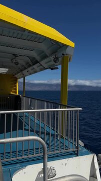 Open passenger ferry deck with railings and structural details overlooking the Atlantic Ocean and distant island landscape in the Canary Islands, Spain.