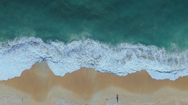Top view beach and ocean waves transparent green sea waters. Drone view of beautiful turquoise sea waves breaking on sandy coastline. Aerial shot of beach meeting deep blue ocean water and foamy waves
