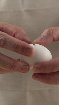 A close-up of a chef's hands cracking a fresh chicken egg with a knife. The process of preparing breakfast or baking