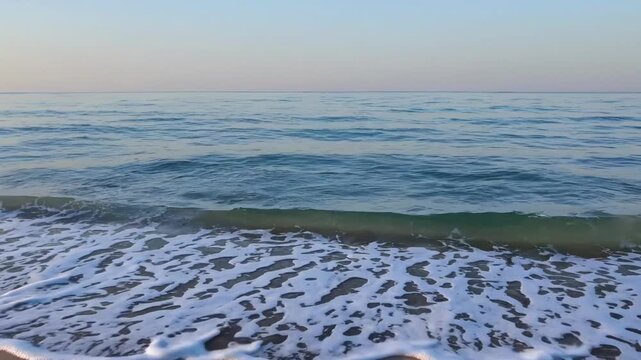 Calm sea waves gently splashing over a sandy shore during a serene sunrise, creating a relaxing and peaceful atmosphere with a beautiful clear sky over the tranquil ocean horizon