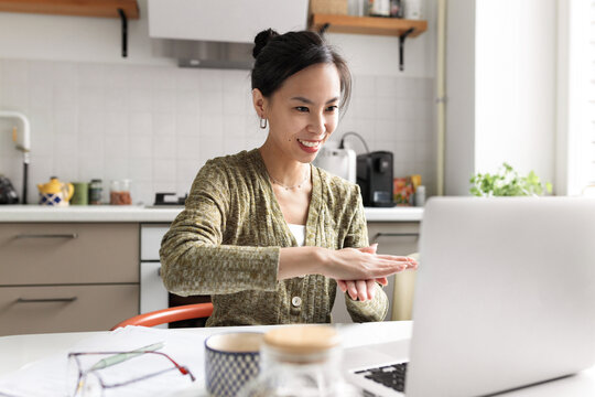 Asian female sign language user working remotely using laptop and online video call application, talking to deaf person gesticulating and smiling, explaining something with gestures