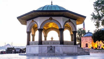 Fototapeta premium A beautifully illuminated historic marble pavilion with ornate arches and a turquoise dome standing proudly in an ancient public square at dusk.