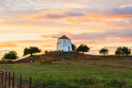 White windmill surrounded by fields beneath pastel sunset clouds