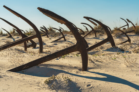 Rows of ancient ship anchors stretch across the beach, creating dramatic shadows