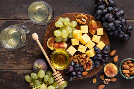 cheese platter with grapes, figs and nuts on wooden background, top view