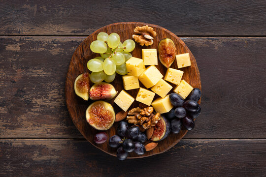 cheese platter with grapes, figs and nuts on wooden background, top view