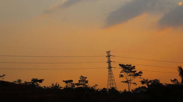 Silhouette of an Electricity Transmission Tower and Power Lines Against an Orange Sunset Sky