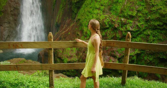 Woman admiring tall waterfall Catarata del Toro from a wooden viewpoint during travel in Costa Rica