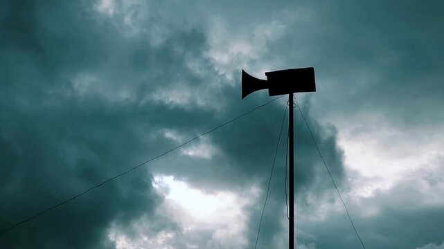 Silhouette profile of a horn loudspeaker set on a high post framed by teal and gray storm clouds, echoing a powerful Islamic azan call to prayer across a broad Muslim community.