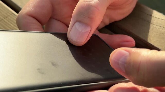 Fingers tapping on screen on dark cellphone. Person holding mobile phone, typing and texting, sending text message in messenger. Close view of hands operating smartphone device at wooden