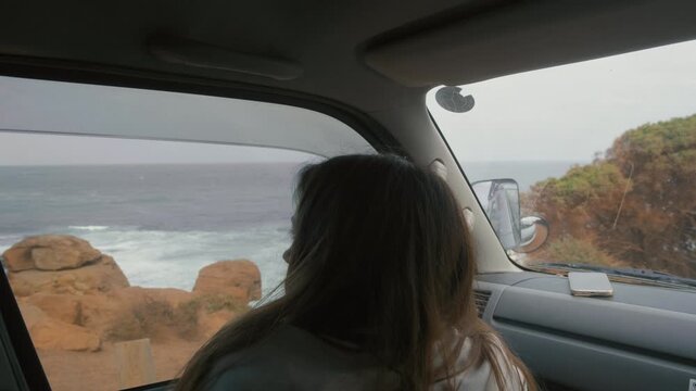 Traveler watches waves crashing on rocks while sitting in a car parked along the scenic Western Australian coastline during the day