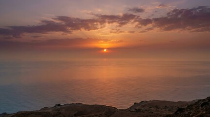 Obraz premium A serene sunset view over the tranquil ocean, featuring warm golden light and soft clouds above the horizon.