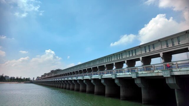 A long concrete sluice structure spans over water, under a bright blue sky with white clouds, showcasing water control infrastructure.