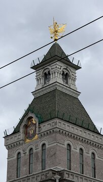Tower with a green tiled roof topped by a golden double-headed eagle emblem against a cloudy sky.