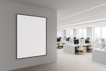 Naklejka premium Empty framed poster mockup on an interior wall overlooking a bright modern office workspace with desks, monitors, and city windows. 3D Rendering