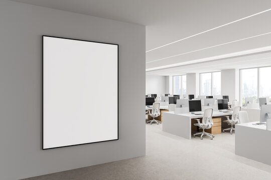 Empty framed poster mockup on an interior wall overlooking a bright modern office workspace with desks, monitors, and city windows. 3D Rendering