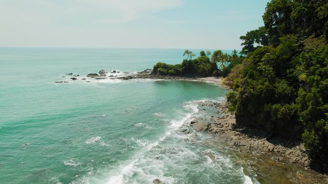 Rocky cove with dense tropical forest beside calm turquoise ocean on sunny day Playa Caballeros Costa Rica