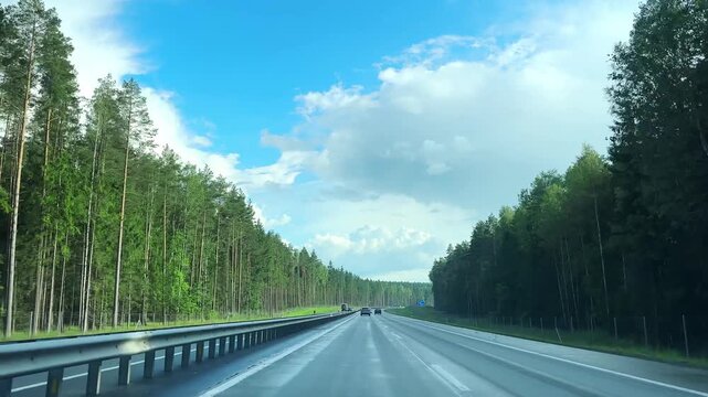 Minsk region Belarus July 7 2026 Fast drive through a wooded highway under a bright sky. Clouds move above the road during a summer journey. Scenic windscreen view captured at speed around