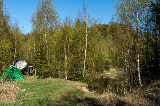 Wild camping site with green tent beside a small forest pond surrounded by young birch trees on sunny spring day. Concept of outdoor adventure, camping, hiking and recreation in nature.