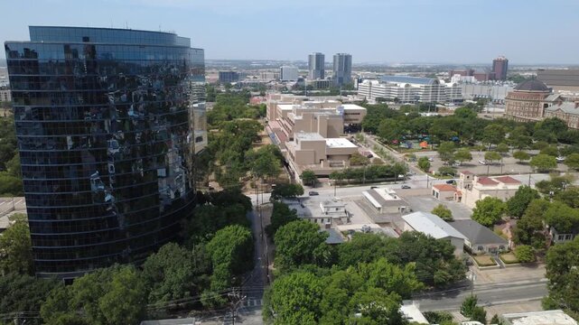 Prominent curved office highrise towers over municipal low rise facilities near Maple Avenue, Dallas. Paved thoroughfares weave through mature green tree rows, DFW Metroplex, Texas
