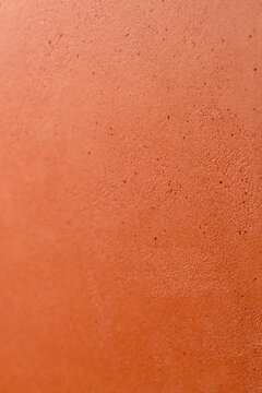 Extreme close-up of a terracotta surface showing detailed porous grain structure and rough matte texture in warm orange-red tones, suitable for material backgrounds and cosmetic product advertising.