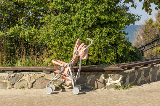 Empty baby stroller beside wooden bench and green trees during daytime