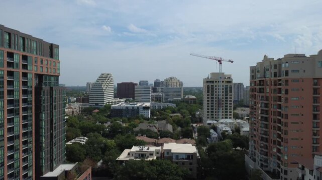 Geometric brick residential highrise overlooks quiet tree lined streets near Oak Lawn, Dallas. Tall tower cranes punctuate sunny skies above growing properties, DFW Metropolitan Area, Texas