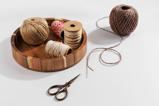 Rustic craft supplies with twine ball, string spools and scissors arranged in wooden tray on minimal background, diy packaging and handmade craft workspace