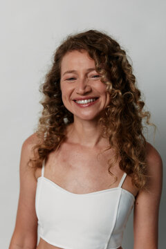 Authentic beauty of a middle-aged woman with natural curly hair and skin without retouching. Smiling mature female portrait against a light background for skincare concepts.