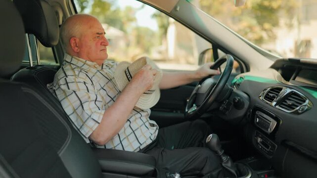 Mature driver feeling hot and fanning himself with a hat inside the summer car.