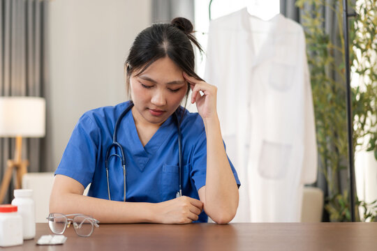A healthcare worker in blue scrubs sits quietly after a demanding shift with a thoughtful expression. The portrait conveys fatigue, burnout, and the need for rest and emotional recovery