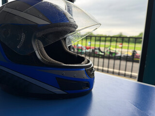 Fototapeta premium A blue racing helmet is placed on a table while go-karts are visible in the background.