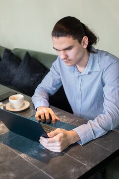 Young man works on laptop while sitting at table in cafe with coffee during daytime