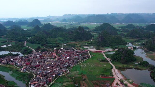 Aerial shot of a clustered rural village nestled among green karst mountains, with rivers and farmland nearby.