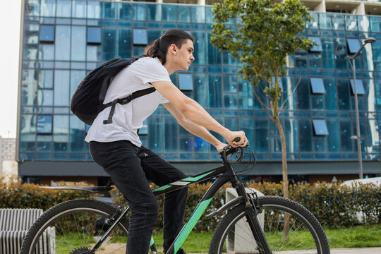 A young man rides a bicycle in a busy city area. Tall buildings surround him as he focuses on the road ahead.