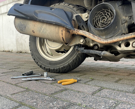 Repairing a scooter on the sidewalk with tools and gloves laid on the ground during the day in an urban area