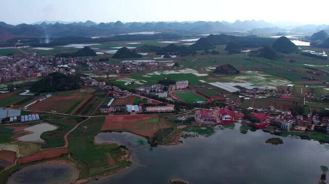 Aerial landscape of a rural area with settlements, farmlands, lakes and karst mountains in the distance.