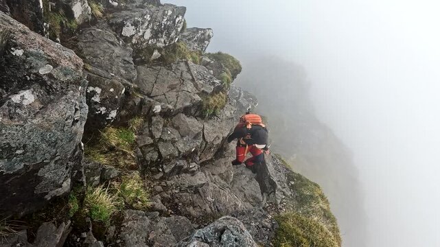 Solo male hiker climbing over exposed Aonach Eagach ridge in the Highlands of Scotland near Glencoe