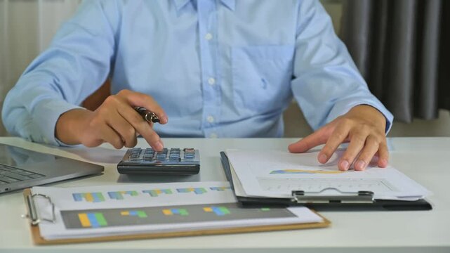 Businessman using calculator and fountain pen to compute financial chart report documents at office desk for corporate accounting budget analysis, audit planning and investment concept