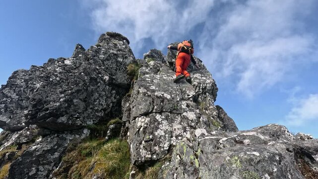 Solo male hiker climbing over exposed Aonach Eagach ridge in the Highlands of Scotland near Glencoe