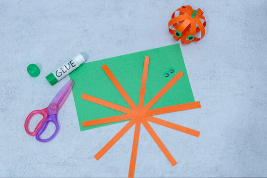 Step 4 of 7 making paper pumpkin for Halloween. Assembling cut paper strips together to shape the round pumpkin for Halloween decoration