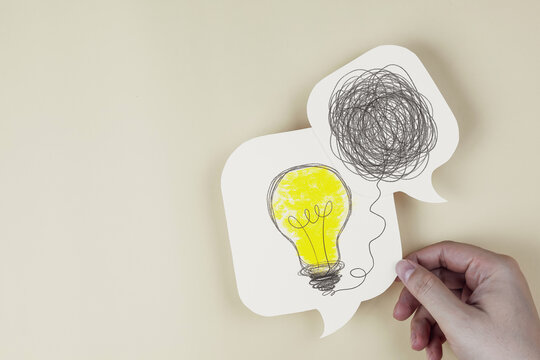 Hand holding speech bubble paper cut with light bulb untangled from messy line scribbles. Concept of problem solving, finding solutions, creative thinking, and mental clarity.
